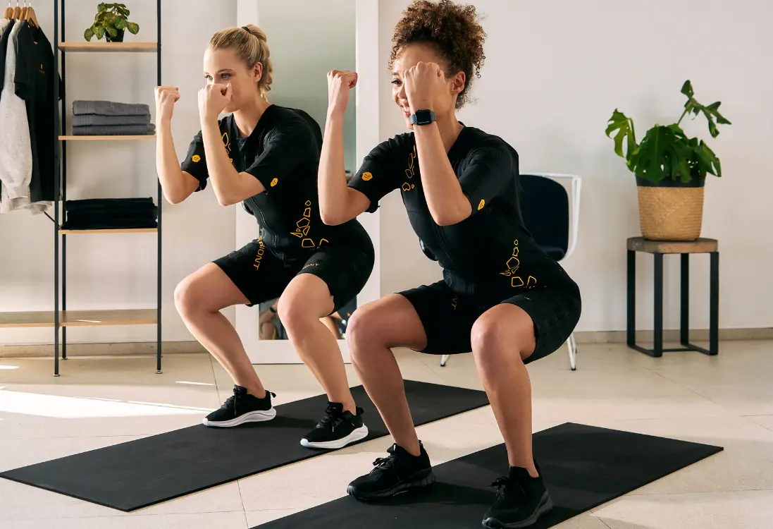 Fast results with EMS training in Pretoria Two women in EMS suits do squats and use EMS training in Pretoria to get quick results in a short time.